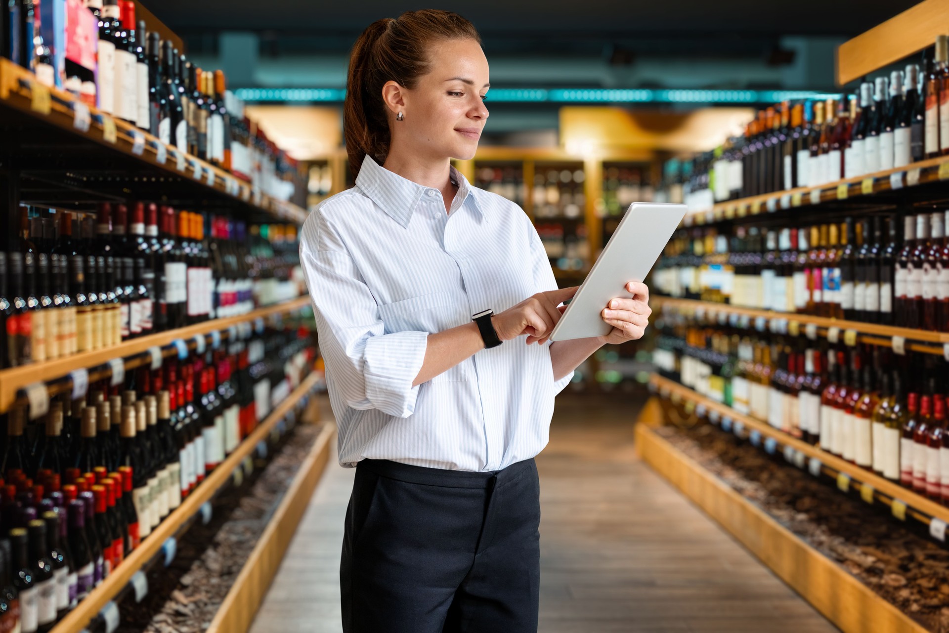 Businesswoman retail manager working on her digital tablet while standing in the wine shop sales area.